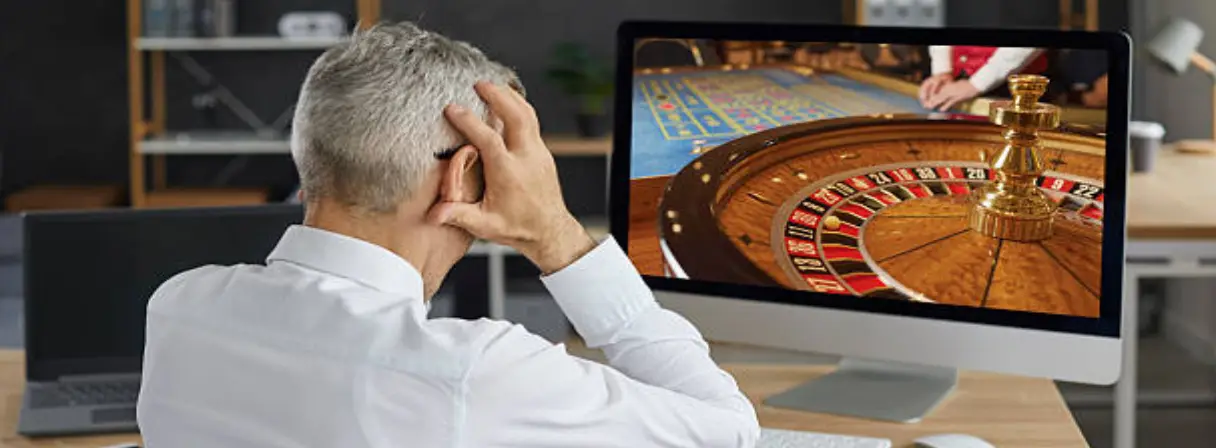 A man looks stressed, holding his head while playing online roulette wheel
